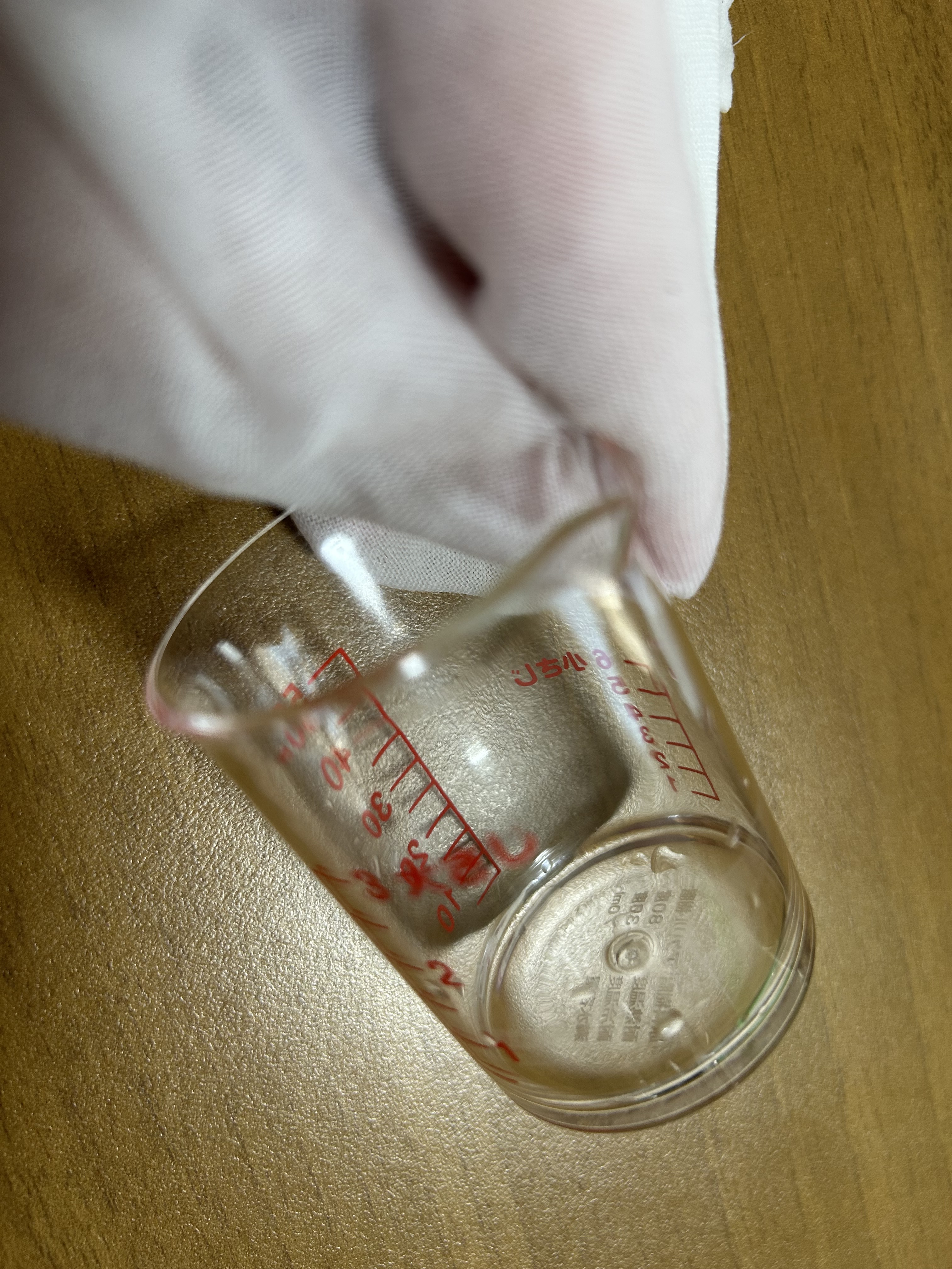 竹布洗顔クロスを濡らして指にまとい計量カップの縁を持っている様子